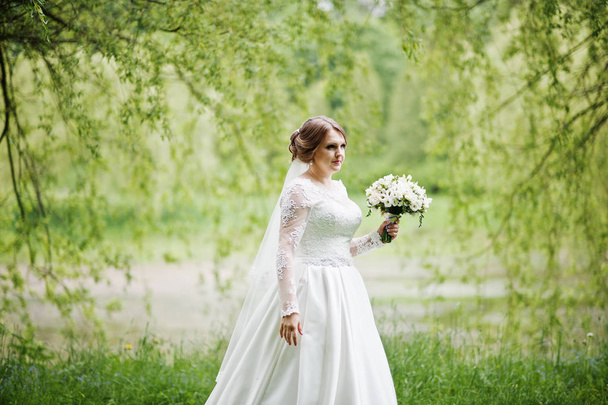 Portrait of a beautiful young bride posing with a bouquet outdoo - Fotó, kép