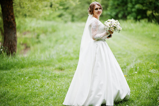 Portrait of a beautiful young bride posing with a bouquet outdoo - Fotó, kép