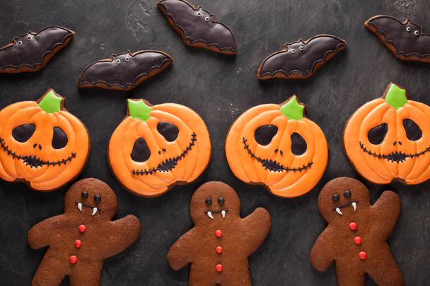 Homemade gingerbread cookies for Halloween in the form of pumpkins, gingerbread men and bats on dark concrete background. Top view - Photo, Image