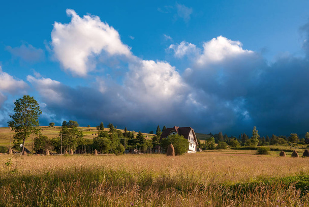 Paisaje rural con pajar en un día soleado de verano. Paisaje rural de montaña con nubes de tormenta
. - Foto, Imagen