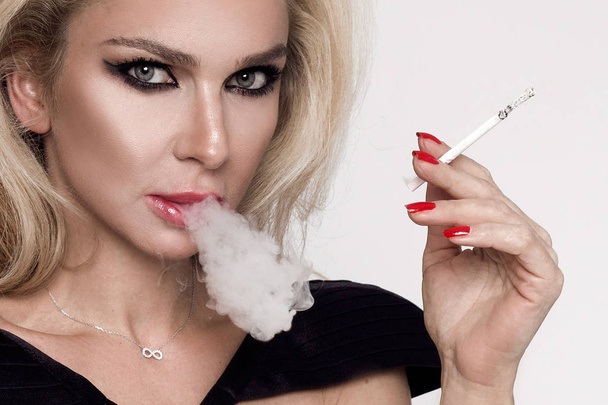 Szexi szőke nő érzéki femme fatale ül a fekete Erotikus fehérnemű és gőzölő egy cigaretta - Fotó, kép