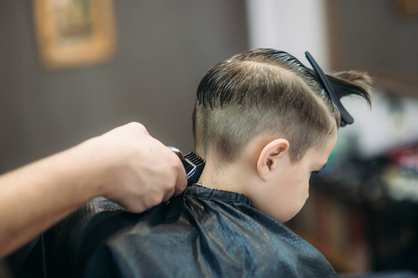 Mały chłopiec coraz fryzura Barber, siedząc w fotelu na fryzjera. - Zdjęcie, obraz