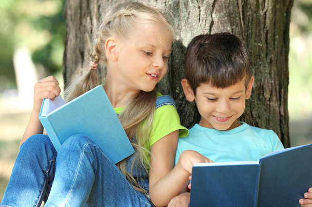 Cute little children reading books near tree in park - 写真・画像