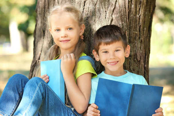 Cute little children reading books near tree in park - Photo, Image