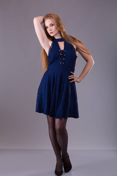 Portrait of a plus size female redhead model posing in blue dress over gray background. - Foto, immagini