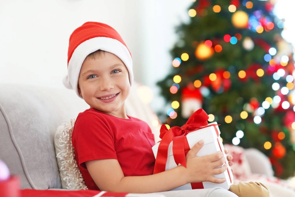 Happy little boy with Christmas gift box sitting on sofa at home - Photo, image