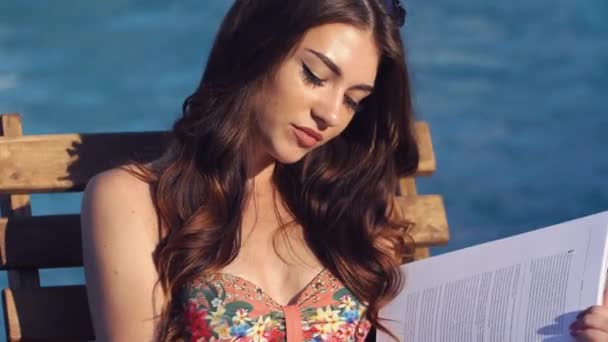 Young beautiful woman reading the book near the swimming pool - Materiał filmowy, wideo