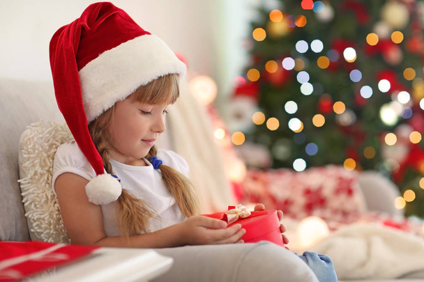 Happy little girl with Christmas gift box sitting on sofa at home - Photo, Image