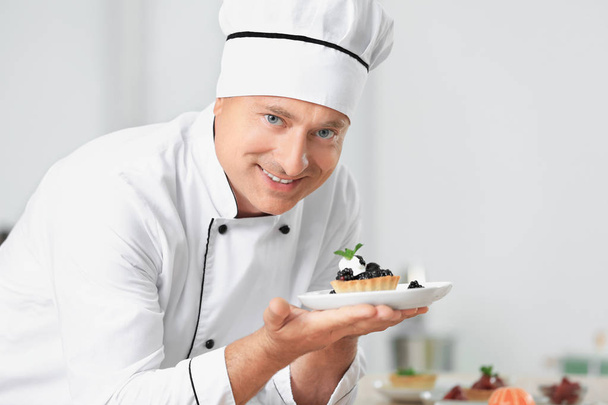 Male chef holding plate with dessert in kitchen - Zdjęcie, obraz