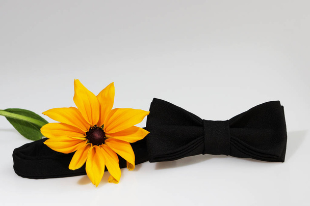 Composition: Extravagant black official classic bow tie and yellow flower on a white background. - Photo, Image