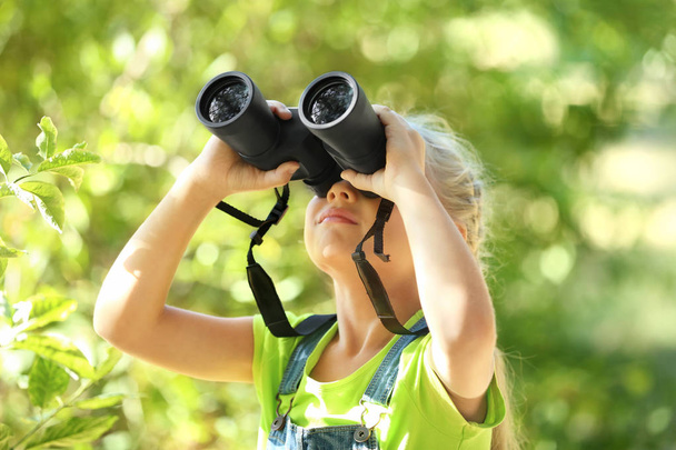 Cute girl looking through binoculars outdoors - Foto, afbeelding