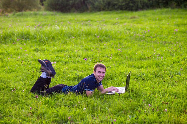 Hombre joven se encuentra en la hierba verde con el ordenador portátil y el trabajo
  - Foto, imagen