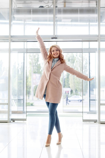 Beautiful blond young girl in a beautiful beige coat, jeans and high heels. - Foto, afbeelding