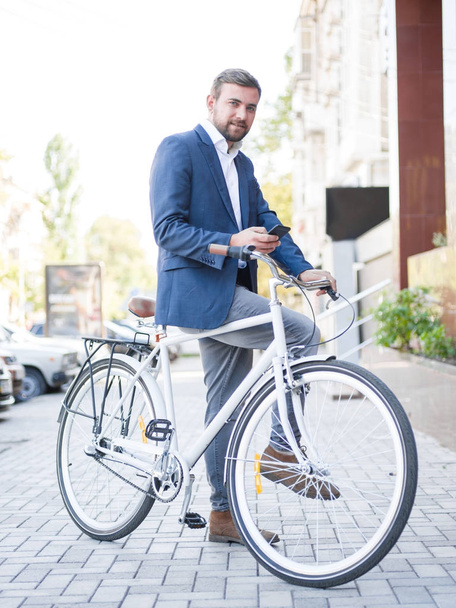 Bearded man with a bicycle, texting on a phone on a city background. Busy life concept. Copy space. - Foto, afbeelding