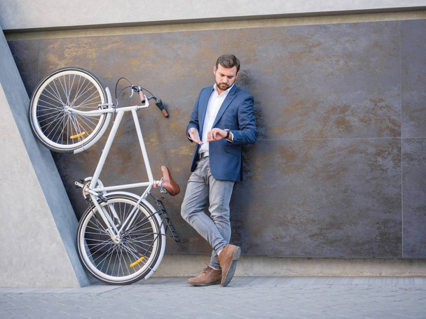 Businessman looks at his phone, next to a bicycle is lifted on his hind legs - Valokuva, kuva