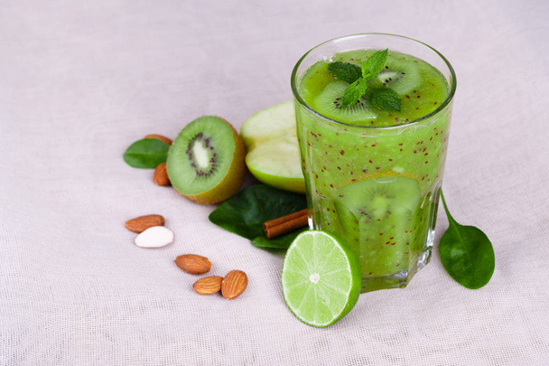 A bright green kiwi smoothie with spicy peppermint and fresh apple on a light table background. Cut in half kiwi with green leaves and nutritious almond nuts. Fruit cocktails for vegetarians. - 写真・画像