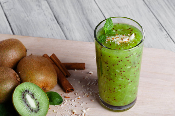 A top view of kiwi fruits full of nutritious vitamins, cinnamon sticks and walnuts on a cutting board and on a gray wooden background. An organic green smoothie from juicy kiwi, grated nuts, and mint. - Valokuva, kuva
