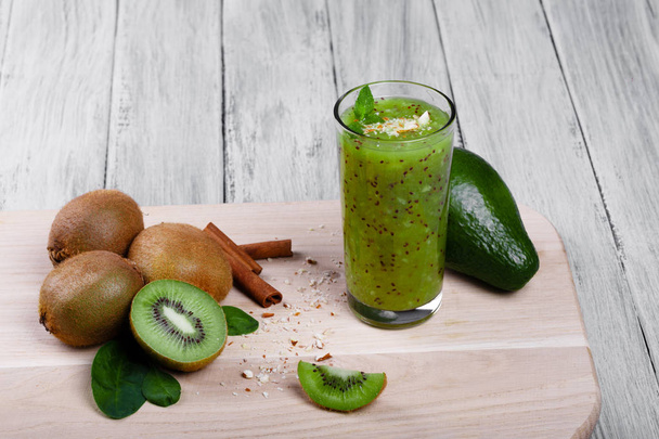 Sweet summer green kiwi drink or smoothie from exotic kiwi fruits, avocado, walnuts, cinnamon and mint on a gray wooden background, close-up. Cinnamon sticks, avocado, and kiwis on a desk. - Foto, afbeelding