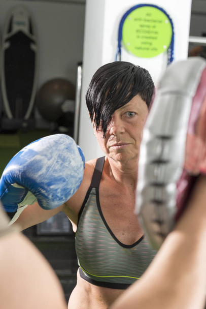 Mujer usando guantes de boxeo mira fijamente una manopla de boxeo
 - Foto, imagen