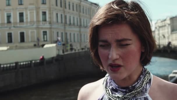 Mujer joven con problemas en vestido moteado canta en la orilla del río en el centro de la ciudad vieja
 - Metraje, vídeo