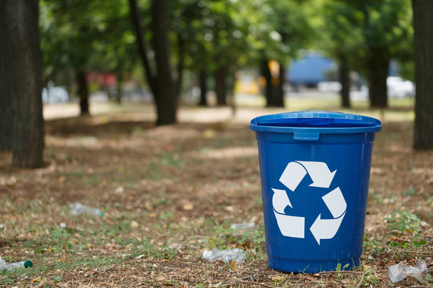 eine helldunkelblaue Wertstofftonne im Park oder Holz. ein bunter Plastikbehälter für das Müllrecycling auf einem unscharfen natürlichen Hintergrund. Umwelt, Ökologie, Naturschutz, Umweltschutzkonzept. - Foto, Bild