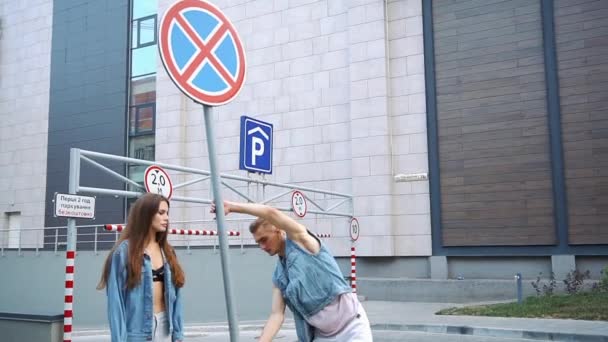 Man shows tricks posing with a lady dressed in casual style before a street sign - Materiał filmowy, wideo