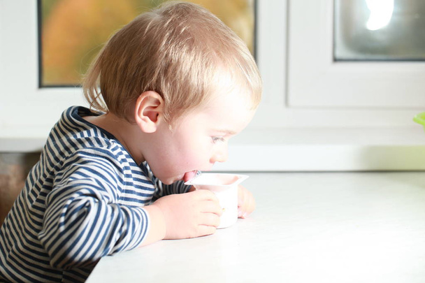 Αστεία μωρό αγόρι Ξανθιές δάχτυλο γλείφει με γιαούρτι - Φωτογραφία, εικόνα