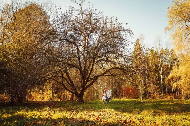 Φθινοπωρινό πάρκο ηλιόλουστη ημέρα με ένα ενιαίο ζευγάρι κάθεται σε μια κούνια - Φωτογραφία, εικόνα