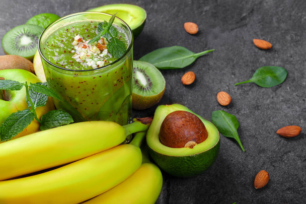 A view from above of a refreshing and exotic smoothie full of vitamins and kiwis on a gray table background. A composition from ripe bananas, organic avocado, mint, cut kiwi and apple on a desk. - Фото, зображення