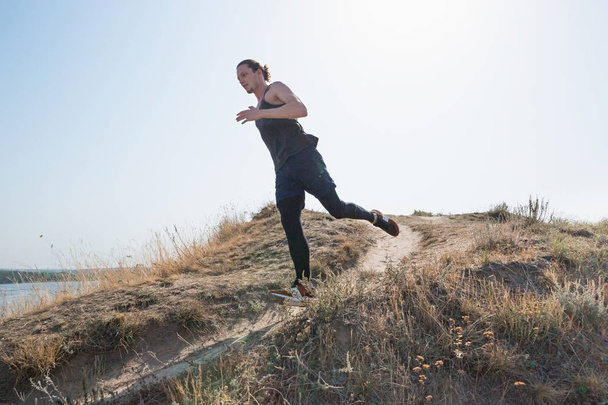 Running sport. Man runner sprinting outdoor in scenic nature. Fit muscular male athlete training trail running for marathon run. - 写真・画像
