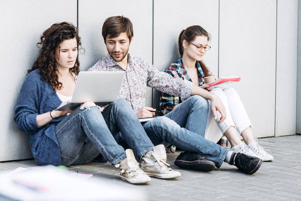 Οι άνθρωποι με βιβλία και gadgets που κάθεται στο πάτωμα κοντά στον τοίχο. Εκπαίδευση κοινωνικών μέσων μαζικής ενημέρωσης έννοια. - Φωτογραφία, εικόνα