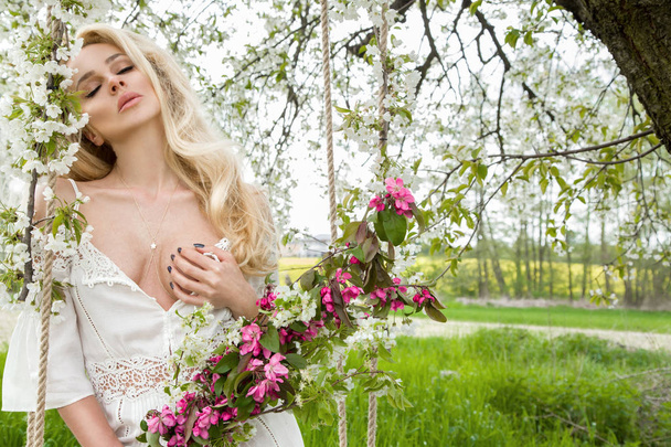 Upea blondi seksikäs luonnollinen nainen keinu keinu puussa yllään kevät mekko tilalla kukkakimppu keväällä
 - Valokuva, kuva
