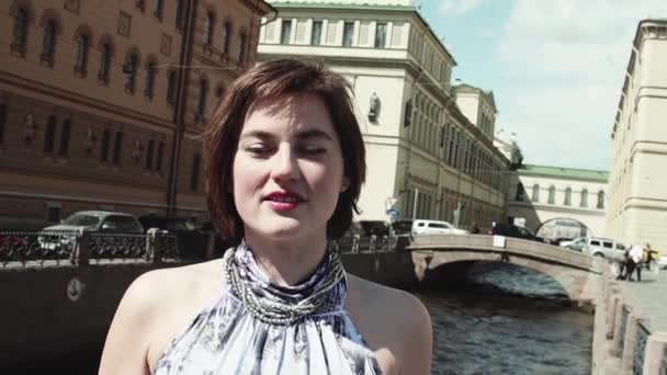 Wesoła dziewczyna w jasną suknię śpiewa wzdłuż rzeki, w centrum starego miasta - Materiał filmowy, wideo
