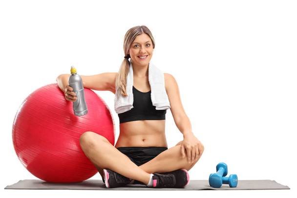 woman with a pilates ball and a bottle sitting on an exercise mat - Valokuva, kuva