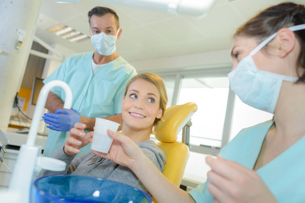 smiling woman is taking a glass of water at dentists - Foto, afbeelding