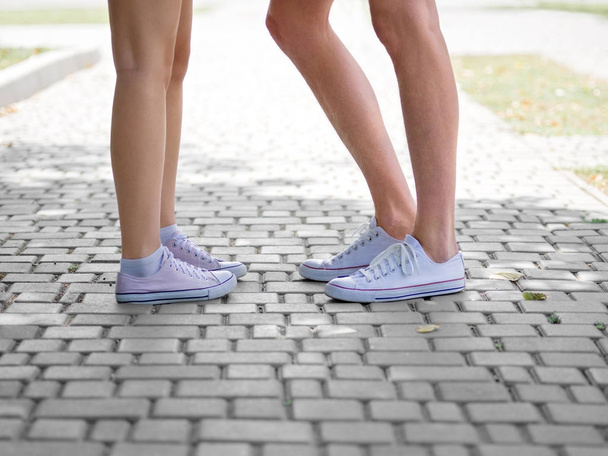Modernas piernas de adolescentes hipster urbano. Una imagen de cerca de las piernas de los adolescentes en zapatos de goma blancos y rosados de pie sobre un fondo empedrado borroso. Copiar espacio. Al aire libre, concepto romántico
. - Foto, Imagen
