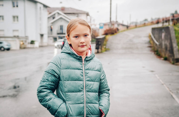 Außenporträt eines hübschen 8-jährigen Mädchens an einem regnerischen Tag mit grüner Jacke - Foto, Bild