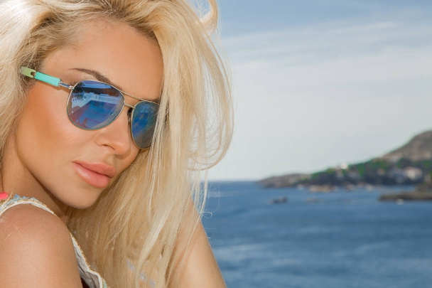 Mulher loira sexy deslumbrante bonita em óculos de sol e roupas elegantes e biquíni ao redor da piscina com vistas incríveis do mar e da Ilha Santorini
 - Foto, Imagem