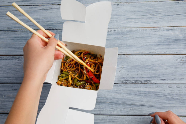 Noodles with chicken and vegetables in a box. Female hands. The concept of food. - Photo, image