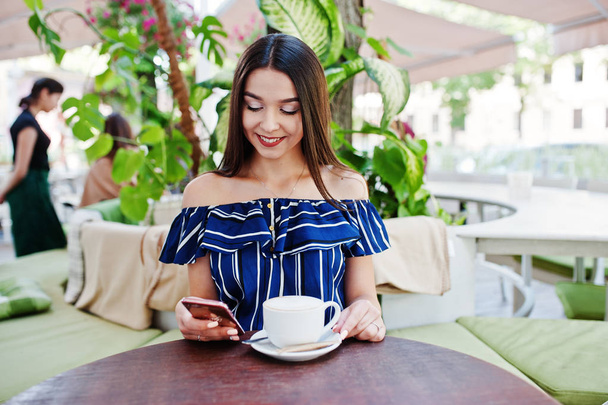 Nádherná brunetka sedící u stolu v kavárně s šálkem  - Fotografie, Obrázek