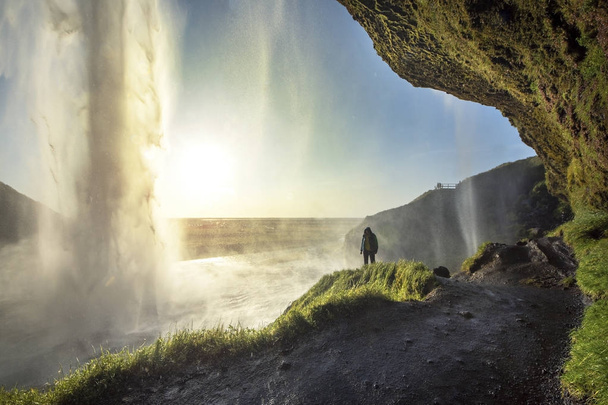 Turista em pé em frente a Seljalandsfoss uma das cachoeiras mais conhecidas no sul da Islândia, Seljalandsfoss, Islândia
 - Foto, Imagem