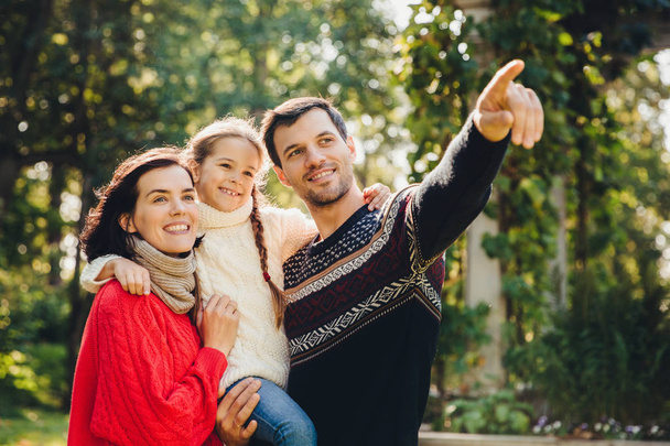 Outdoor portrait of smiling happy friendly family have walk together. Affectionate father shows his small daughter something into distance. Family admire sunrise, beautiful nature, wear warm clothes - Photo, Image