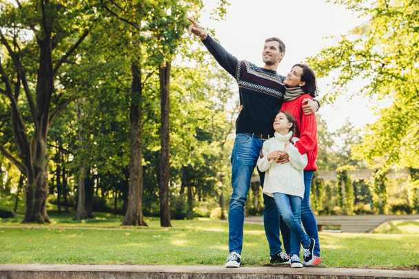 Snímek šťastné radostné mladá rodina otec, matka a malá dcera hrát spolu na podzim park, krajinu, krás venku. Atraktivní muž ukazuje něco s rukou Dcera a manželka - Fotografie, Obrázek