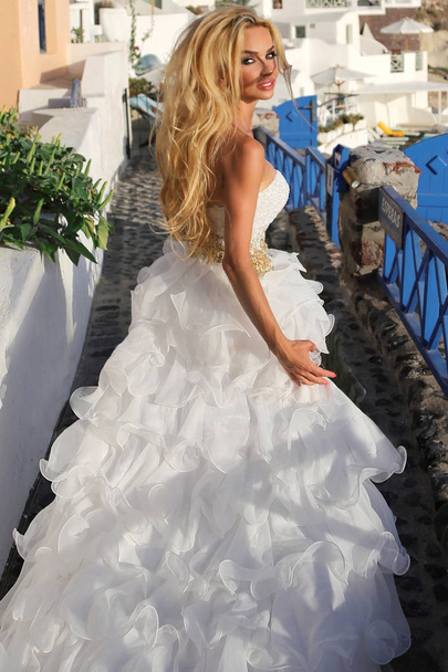 Beautiful bride, blonde model in amazing wedding dress runs to Santorini in Greece. Fleeing bride - Foto, imagen