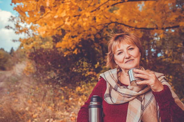 Kobieta w średnim wieku pije herbatę w lesie jesienią - Zdjęcie, obraz
