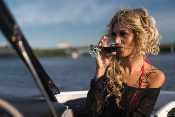 Portrait of attractive woman relaxing on yacht enjoying glass of wine on blue sky sea outdoors. Enjoyment and luxury lifestyle - Valokuva, kuva