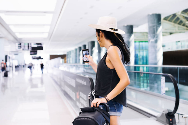 Travel woman using smartphone at airport. Young eastern traveler makes photo with mobile phone app - Фото, изображение