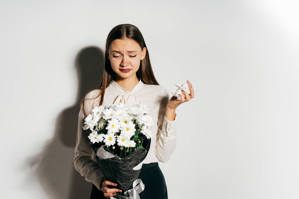 Frustrated girl with a bouquet of flowers on a white background - Фото, изображение