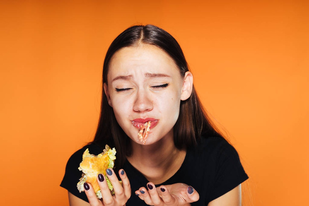 frustrated girl eats a burger in her hands on an orange background - Foto, immagini