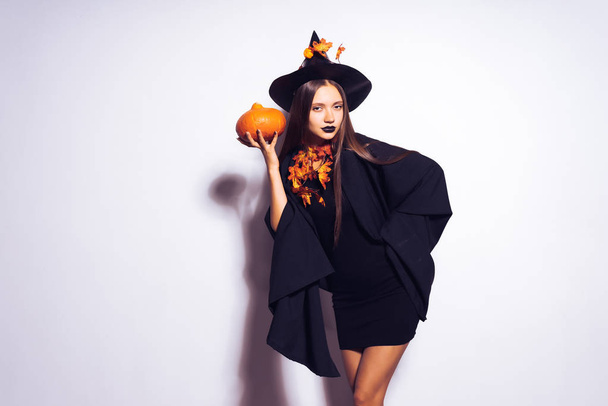 girl in a witch suit holds a small pumpkin in the hands on a white background - Foto, immagini